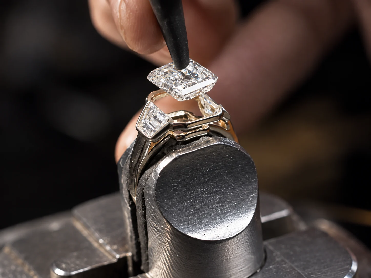 A jeweler positioning a center stone above a custom ring setting